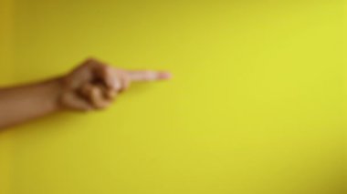 Parlak sarı bir arkaplanı işaret eden el uzatılmış bir parmağın hareketini yakına çekiyor..