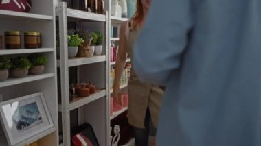 Dekor dükkanındaki kadın ve erkek, çeşitli ev dekorları ürünleriyle çevrili paket teslimatı için imza atıyor, etkileşimlerini ve depolama iç düzenlerini vurguluyorlar.