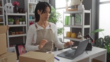 Ev dekorasyonu dükkanında dizüstü bilgisayarlı kutular paketleyen kadın, fabrikalarla ve şık dekorasyonlarla dolu modern çalışma alanı, ambalaj ürünlerine odaklanmış.