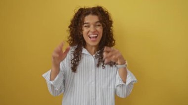 Genç İspanyol kadın heyecanla ayakta duruyor ve başarıyı kutluyor izole edilmiş sarı arka plan, zafer ve mutluluğun neşeli ifadesi