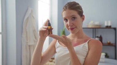Sarışın, güzel bir kadın spa sağlık merkezinde küçük bir şişe yağ tutuyor.