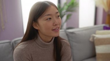 Evinde rahat bir oturma odasında, yumuşak ışıklandırma ve modern dekorla konuşan rahat bir ortamda mutluluk ve rahatlığı ifade eden hoş bir sohbete girişen genç bir kadın..