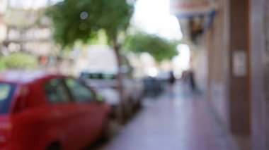 Yoğun bir şehir sokağının arka planı bulanık. Arabalar kenara park edilmiş ve yayalar yürüyor. Odaklanamayan ve bokeh etkisi yaratıyor..