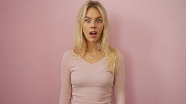 Şaşırmış yüzlü çekici sarışın kadın izole edilmiş pembe arka plan duvarına karşı duruyor.