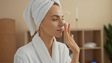 Kaplıca odasında kafasında havluyla ve bornozuyla güzel bir sarışın kadın. Kapalı mekanda rahatlatıcı bir güzellik tedavisinin tadını çıkarıyor..