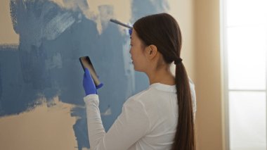 Yeni evde duvarları boyayan bir kadın telefona danışıyordu. Kapalı mekanda eldivenler giyiyordu. Modern estetiği yansıtıyordu..