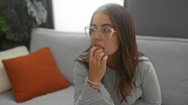 Kapalı bir yerde, gözlüklü bir kadın rahat bir oturma odasında, rahat ve modern bir ev dekorasyonu sergiliyor..