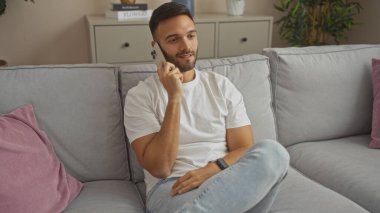 Yakışıklı, sakallı, evinde rahatça otururken telefonuyla konuşan bir adam..