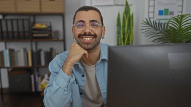 Gözlüklü ve bıyıklı genç bir İspanyol. Ofis ortamında gülümsüyor. Arkasında düzenli bir masa ve kitaplık var.