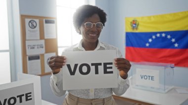 Kıvırcık saçlı Afro-Amerikalı bir kadın, kapalı bir seçim odasında arkasında Venezuela bayrağı olan bir oy pusulası tutuyor..