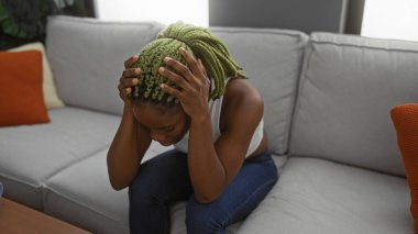 Oturma odasındaki bir kanepede oturan yeşil örgülü ve kederli yüzüyle rahat bir apartman dairesinde duygularını ileten bir kadın..