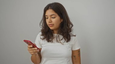Beyaz gömlekli, esmer, genç, güzel, beyaz bir duvar arkasında kırmızı bir telefon tutan bir kadın..