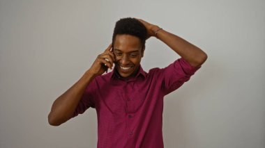 Akıllı telefondan konuşan, beyaz arka planda konuşan pembe gömlekli, eli başının arkasında mutlu ve rahat görünen bir adam.