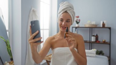 Sağlık merkezinde spa 'da selfie çeken bir kadın kafasında havluyla yağ şişesi tutuyor.