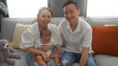 Anne ve baba, bir apartman dairesinde küçük çocuklarına sevgiyle gülümsüyor mutlu bir Çinli aile sergiliyor ve sıcak ve sevgi dolu bir ev ortamı yaratıyorlar..