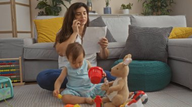 Kız rahat oturma odasında oyuncaklarla oynarken, kadın telefonda konuşuyor ve belgeleri okuyor..