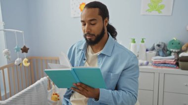 Bebek odasında oyuncaklar ve pastel dekorlarla dolu kitap okuyan genç bir adam. Rahatlama ve öğrenme üzerine odaklanmış sakin bir aile sahnesi sergiliyor.