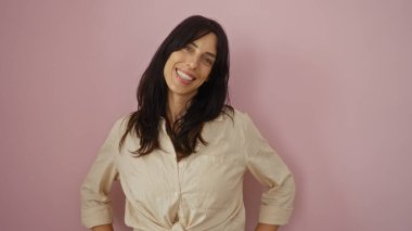 İzole edilmiş pembe bir arka plan karşısında gülümseyen İspanyol genç bir kadın. Çekici ve doğal görünüşüyle kendine güveni ve güzelliği yayıyor..