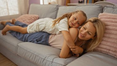 Anne ve kızı sıcak bir aile bağı ve ev rahatlığı sergileyerek, parlak bir oturma odasında rahat bir kanepede dinleniyorlar.