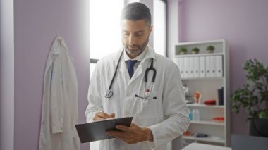 Doktor parlak bir hastane odasında notlar yazıyor, beyaz önlük ve steteskop giyiyor, arka planda raflar ve bitkiler var, profesyonellik ve sağlık ortamını gösteriyor..