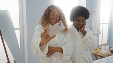 Women friends taking selfie together in spa salon wearing robes smiling in wellness center clipart