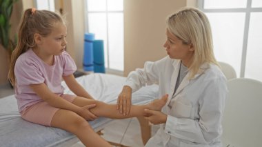 Kadın fizyoterapist bacak yaralanması için klinikteki çocuk hastasını tedavi ediyor.