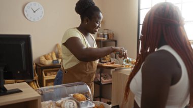 Pasta dükkanında müşteriye servis yapan kadın, arka planda ekmek, gülümseyen ve nişanlı kadınlar.