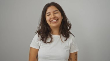 Çekici, Latin kökenli, esmer bir kadın, izole bir ortamda beyaz bir arka plan duvarından gülümsüyor..