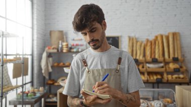 Defterine sakallı genç adam çeşitli ekmek ve hamur işleriyle dolu bir pastanede dikilirken....