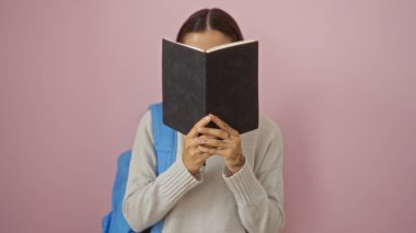 Pembe arka planda dururken kitap okuyan genç bir kadın..