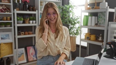 Ev dekorasyonunda gülümseyen sarışın kadın. Arka planda çeşitli dekorasyonlar var.