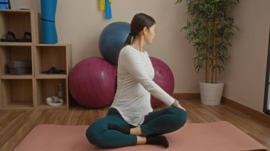 Spor salonunda yoga yapan bir kadın spor salonunda spor topları ve bambu bitkisiyle spor yapıyor. Spor ve sağlık etkinliği için sakin bir iç mekan yaratıyor.