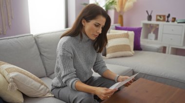 Şık oturma odasındaki kanepede mektup okuyan bir kadın. Yastıklı, modern dekorlu, rahat bir dairesi olan..