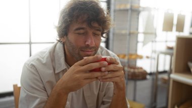 Yakışıklı genç adam bir fırının içinde kahveden zevk alıyor, sıcak, güneşli bir yerde otururken aromanın tadını çıkarıyor..