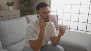 Evde modern bir oturma odasında otururken sakallı yakışıklı bir İspanyol adam telefonuyla konuşuyor..