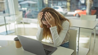 İşyerinde kafası tutulmuş bir kadın, pencerenin önünde oturmuş, laptopu ve kahve masasının üzerinde modern iç ve dış görünüşle çevrili bir şekilde oturuyor.