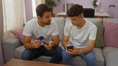 Baba oğul akıllı telefonları ve kredi kartlarını kullanarak sıcak bir oturma odasındaki kanepede otururken kapalı alanda sevgi dolu bir aile anını sergiliyorlar.