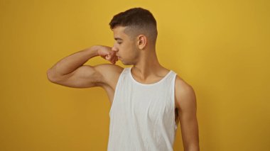 Beyaz atletli genç İspanyol adam kollarını esnetiyor, canlı sarı bir arka plana yaslanıyor, zindelik ve güç gösterisi yapıyor..