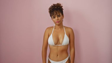 Beyaz mayo giymiş kıvırcık saçlı esmer kadın izole edilmiş pembe arka plana karşı poz veriyor.