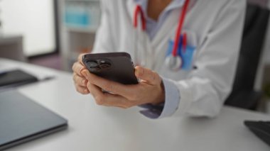 Klinikte akıllı telefon kullanan, beyaz önlüklü, elleri ve mobil cihaz etkileşimine odaklı tıbbi profesyonel ortam öneren bir kadın..