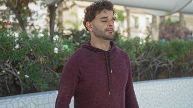 Yakışıklı, gözleri kapalı, şehir parkında güneşli bir günde çevresi yeşillik ve şehirlerle çevrili olan yakışıklı bir İspanyol.