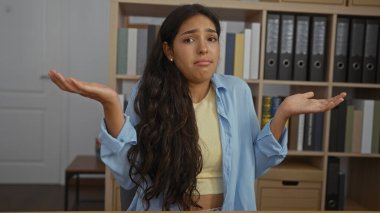 Ofis çalışma odasında arka planda kitaplıklarla omuz silken bir kadın belirsiz ve kafası karışmış görünüyor.