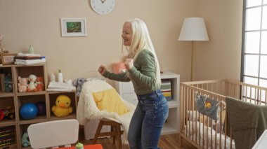 Albinizmli bir kadın, bebek beşiği ve oyuncaklarıyla rahat bir yatak odasında neşe içinde dans ediyor. Kapalı mekanda mutluluk ve sıcaklığı terbiye ederken görülüyor..