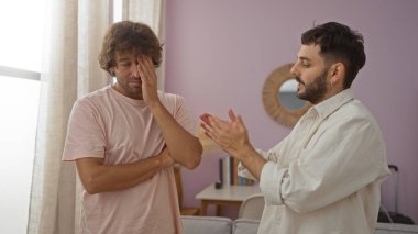 Oturma odasında iki adam gergin bir konuşma yapıyor gibi görünüyor. Biri stresli görünüyor diğeri de elleriyle işaret ediyor..