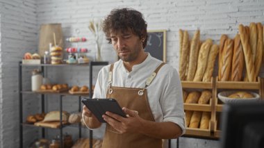 Taze ekmek ve hamur işleriyle çevrili bir dükkanda tablet kullanan İspanyol bir adam.