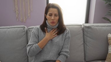 Kadın rahat bir oturma odasında, rahat bir dekor ve mor duvarları olan koltukta otururken rahat hissetmiyor ev ve sıcaklık duygusunu aktarıyor..