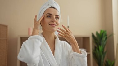 Kaplıca merkezinde beyaz bornoz ve havluyla gülümseyen beyaz bir sarışın kadın.