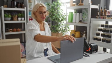 Dizüstü bilgisayarda çalışan bir kadın dekoratif eşyalar ve bitkilerle çevrili bir mağazada rahat bir alışveriş atmosferi sergiliyor..