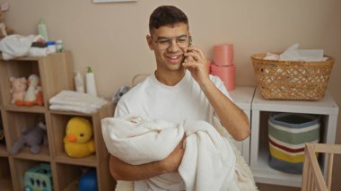 Bebek odasında kucağında yeni doğmuş bir bebekle oyuncaklarla ve mobilyalarla telefonda konuşan genç bir adam, evin içinde rahat bir ortamda yuva kuran bir aileyi öneriyor..