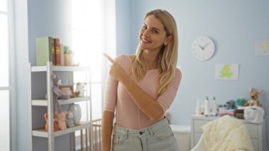 Gösterişli yatak odasında oyuncaklarla gülümseyen, parlak ışık ve çağdaş tasarım ile karakterize edilmiş kapalı bir ortam gösteren bir kadın..